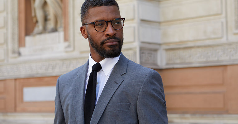 Model wearing black knitted tie, white tab collar shirt and grey suit