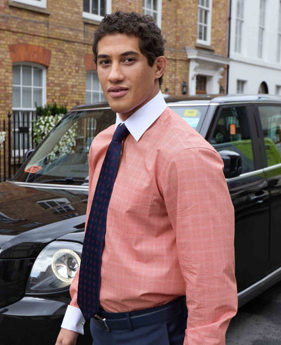 Man wearing a Red and White prince of wales check shirt and dark tie standing in front of a black car.